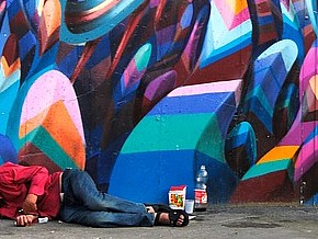 Homeless person beside graffiti wall